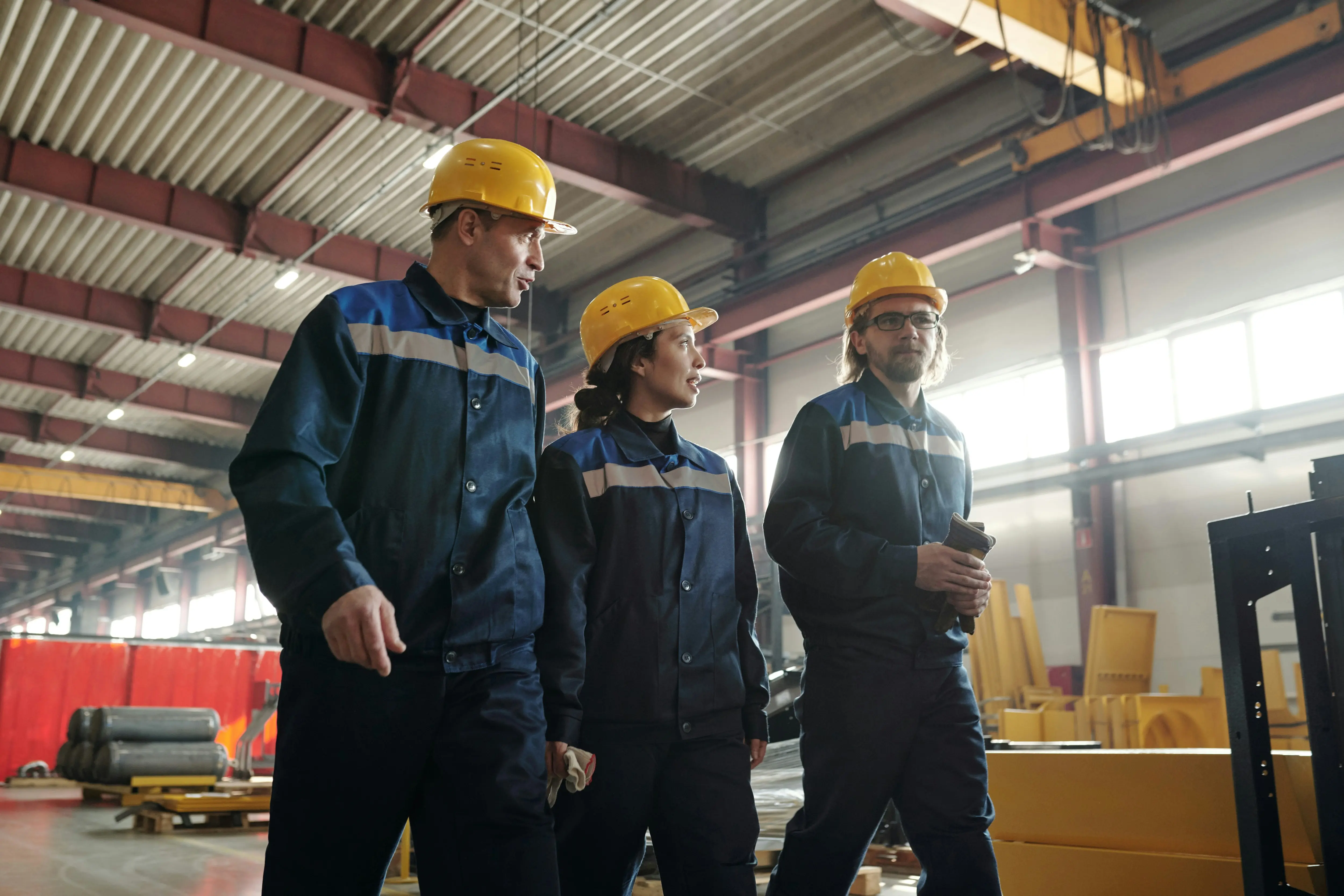Professional workers in blue industrial uniforms with reflective stripes and yellow hard hats in industrial setting